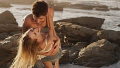 Playful young couple hugging on rocks at ocean — Stock Photo