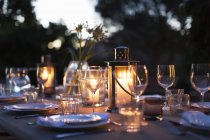 Candles in lanterns on patio dining table with place settings — Stock Photo