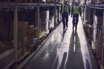 Workers walking along merchandise on shelves in distribution warehouse aisle — Stock Photo