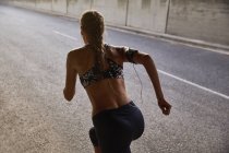 Fit female runner in sports bra and mp3 player armband running on urban street — Stock Photo