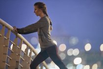 Визначений жіночий бігун розтягує ноги на пішохідному мосту на світанку — стокове фото