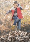Захоплюючий хлопчик стрибає через купу осіннього листя — стокове фото