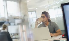 Empresario creativo bebiendo café, trabajando en el ordenador portátil en la oficina - foto de stock