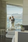 Reflexão de abraços de casal na varanda de luxo com vista ensolarada do oceano e da montanha — Fotografia de Stock