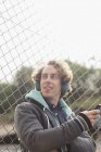 Homme écoutant des écouteurs contre une clôture à maillons de chaîne — Photo de stock
