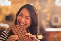 Portrait Chinese woman with sweet tooth craving biting into large chocolate bar — Stock Photo