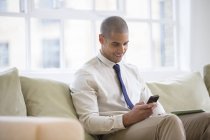 Businessman using cell phone on sofa at home — Stock Photo