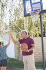 Abuelo y nieta chocan los cinco en el aro de baloncesto - foto de stock