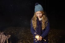Girl playing with sparkler outdoors at nighttime — Stock Photo
