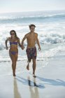 Glückliches Paar hält Händchen und rennt am Strand — Stockfoto