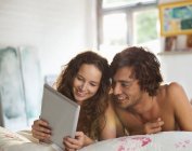 Jovem casal usando computador tablet na cama — Fotografia de Stock