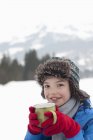 Retrato de menino sorridente bebendo chocolate quente no campo nevado — Fotografia de Stock