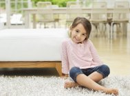 Улыбающаяся девушка сидит на ковре — стоковое фото