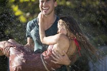 Caucasian happy couple playing in sprinkler in backyard — Stock Photo