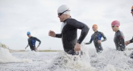 Confident and strong triathletes in wetsuits running in waves — Stock Photo