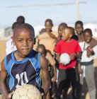 Niños africanos sosteniendo pelotas de fútbol en el campo de tierra - foto de stock