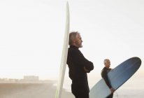 Старший серфер, опирающийся на борт на пляже — стоковое фото