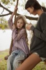 Mãe trançando o cabelo da filha no balanço à beira do lago — Fotografia de Stock