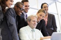 Gli uomini d'affari sorridenti che condividono il computer portatile in riunione a ufficio moderno — Foto stock