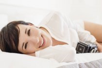 Портрет улыбающейся женщины с винтажной камерой в постели — стоковое фото
