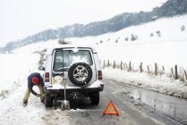 Mann arbeitet im Schnee an kaputtem Auto — Stockfoto