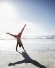 Man in swim trunks doing handstand on beach — Stock Photo
