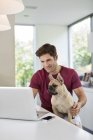 Человек использует ноутбук с собакой на коленях в современном доме — стоковое фото