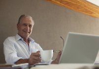 Older man having cup of coffee at desk — Stock Photo