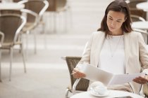 Серйозна бізнес-леді читає документи в тротуарному кафе — стокове фото