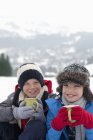 Retrato de chicos sonrientes bebiendo chocolate caliente en el campo cubierto de nieve - foto de stock