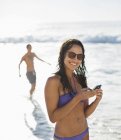 Портрет улыбающейся женщины в бикини с телефоном на пляже — стоковое фото