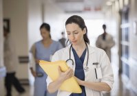Doctor looking down at folder in hospital corridor — Stock Photo