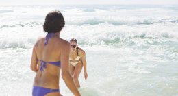 Счастливые друзья в бикини играют в океане — стоковое фото