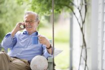 Man talking on cell phone in porch swing — Stock Photo