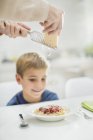 Mother grating cheese over son's spaghetti — Stock Photo