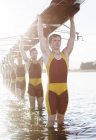 Rowing team carrying boat overhead on lake — Stock Photo
