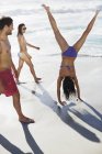 Amigos assistindo mulher de biquíni fazendo suporte na praia — Fotografia de Stock