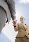 Бізнесмен і бізнес-леді потискають руки під блакитним небом — стокове фото