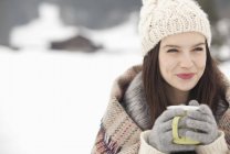 Nahaufnahme einer lächelnden Frau mit Strickmütze und Handschuhen, die im verschneiten Feld Kaffee trinkt — Stockfoto