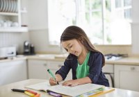 Menina usando livro de colorir na cozinha — Fotografia de Stock