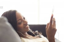 Jeune femme attrayante écoutant des écouteurs sur le canapé — Photo de stock