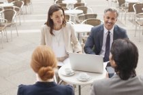 Smiling business people with laptop meeting at sidewalk cafe — Stock Photo