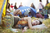 Mujer con tiara durmiendo en saco de dormir fuera de tiendas de campaña en el festival de música - foto de stock