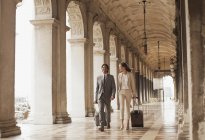 Homme d'affaires souriant et femme d'affaires tirant des valises le long du couloir à Venise — Photo de stock
