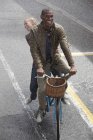 Happy multiracial couple riding bicycle in rainy street — Stock Photo