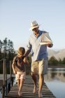 Дедушка и внук с игрушечным парусником прогуливаются вдоль причала через озеро — стоковое фото