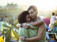 Couple in sleeping bag hugging outside tents at music festival — Stock Photo