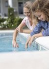 Madre e hija sumergiendo los dedos en la piscina - foto de stock