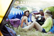 Друзья с гитарой тусуются возле палаток на музыкальном фестивале — стоковое фото