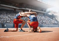 Runners huddled and kneeling on track — Stock Photo